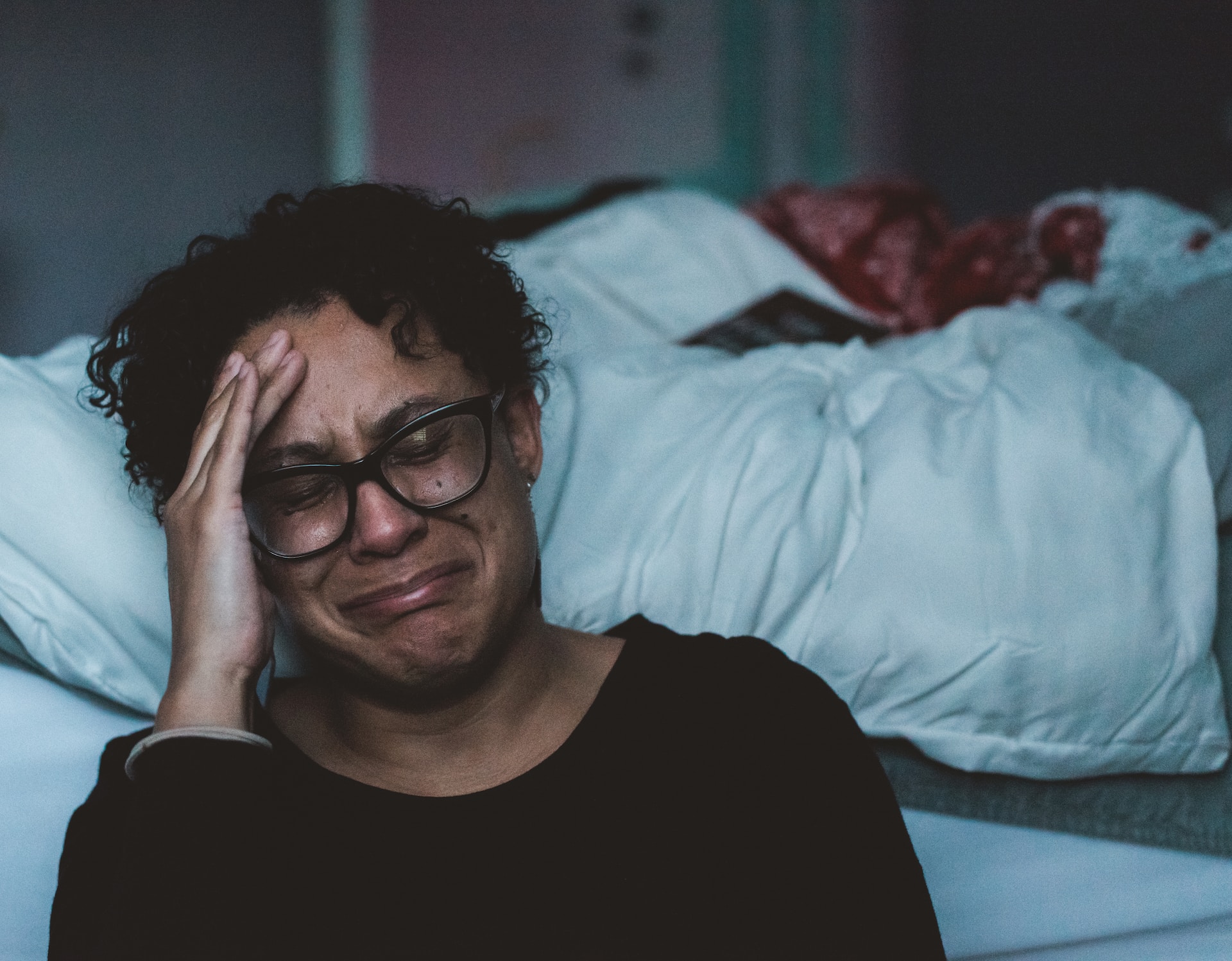 A grieving woman is seen crying while beside a bed. Source: Claudia Wolff on Unsplash.