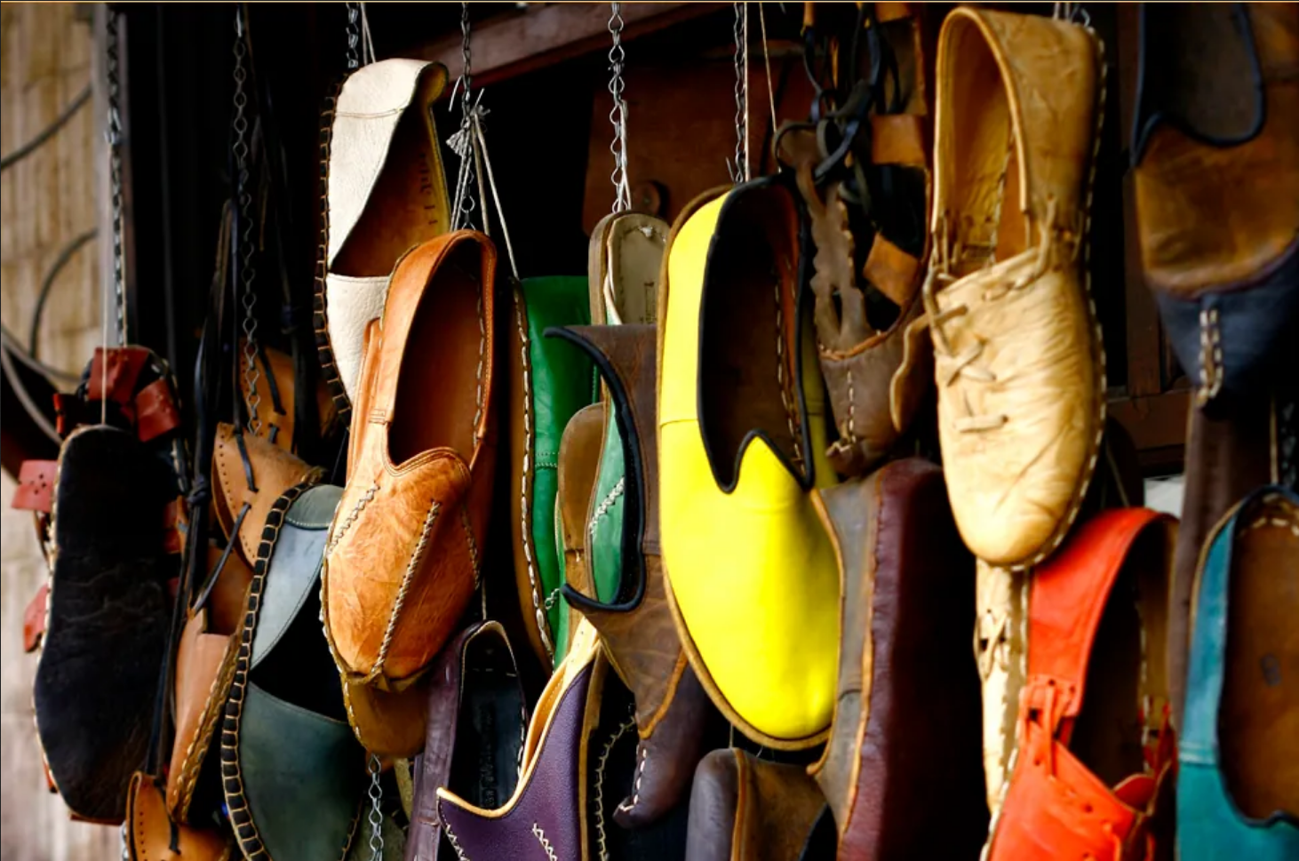 This photo shows many different pairs of shoes in various colors. The shoes appear to be hanging from a wall by cords.