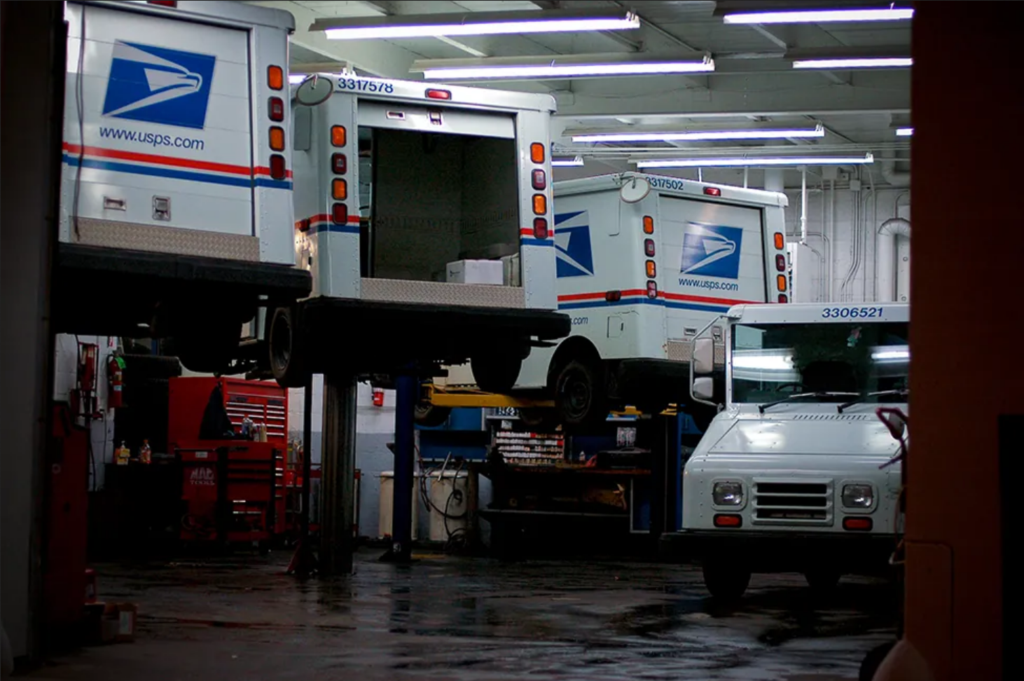 A car mechanic’s shop. There are three United States Postal Services trucks being serviced, and one not being serviced.