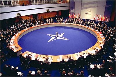 NATO summit 2002. Image is of representatives sitting around the large round table with NATO symbol in middle. 