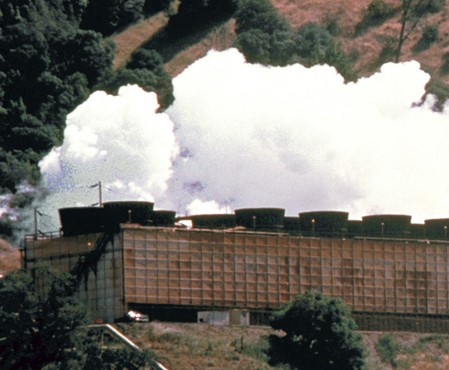 An energy plant on a hillside with clouds of white steam 