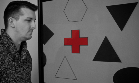 A photograph shows a person staring at a screen that displays one red cross toward the left side and numerous black and white